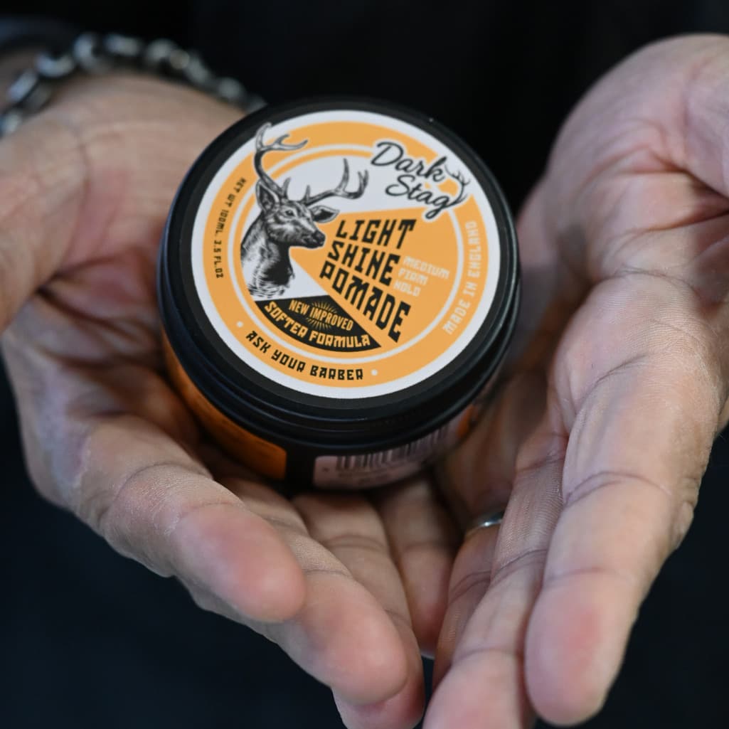 Person holding a jar of 'Dark Stag' light shine pomade.