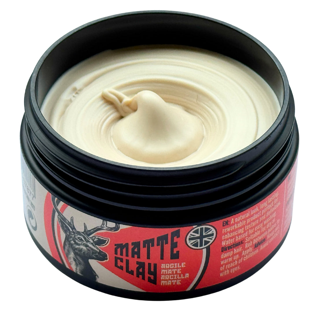 A jar of Matte Clay hair styling product, showing the creamy off-white clay texture inside a black container with a red and black label featuring a deer graphic.