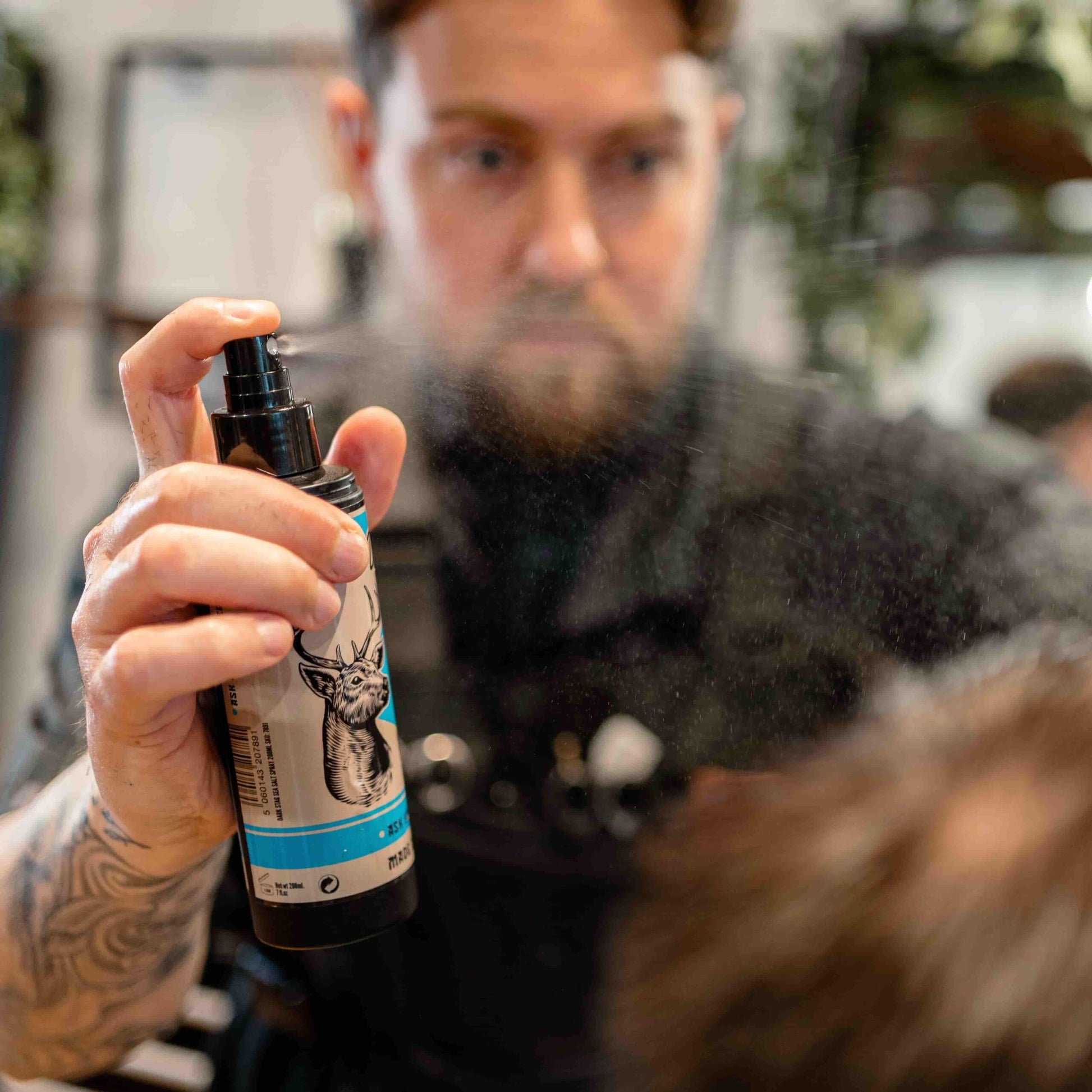 Man holding a hair product spray bottle in a salon setting