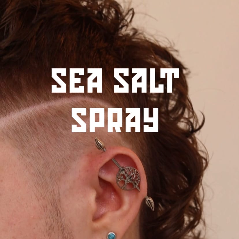 Close-up of an ear with a tree-shaped earring, text 'SEA SALT SPRAY' on a plain background