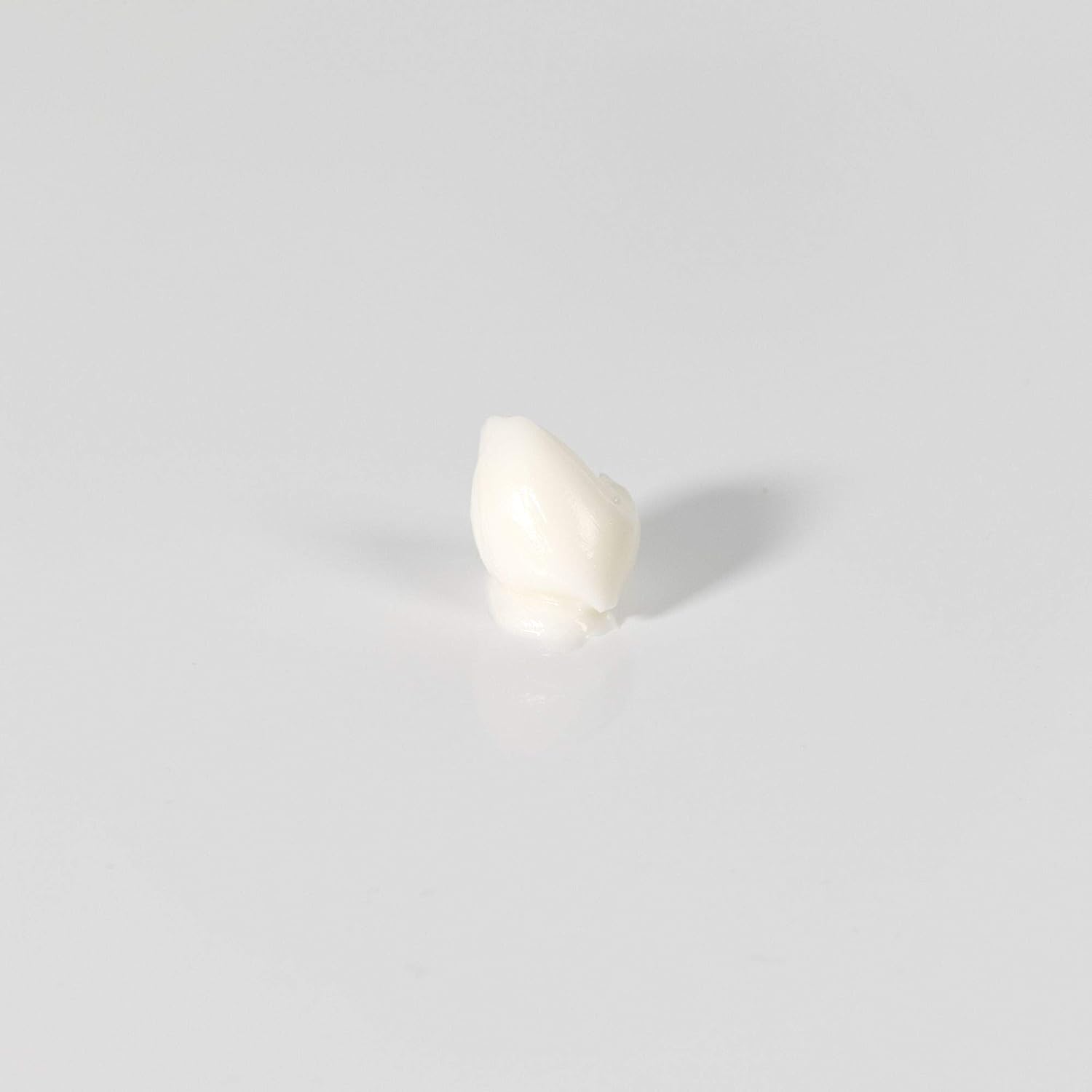 A single small off-white tooth-shaped object centered on a plain light gray background.